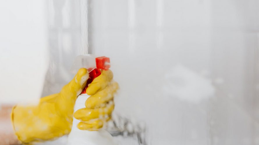 person in glove spraying detergent at walk in shower glass