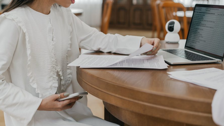 a woman sitting near the wooden table while holding papers and mobile phone