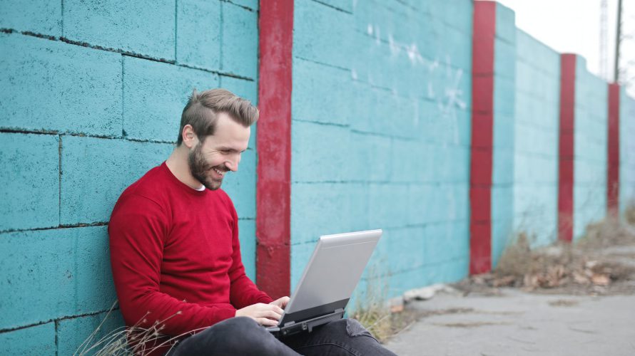 man leaning against wall using laptop